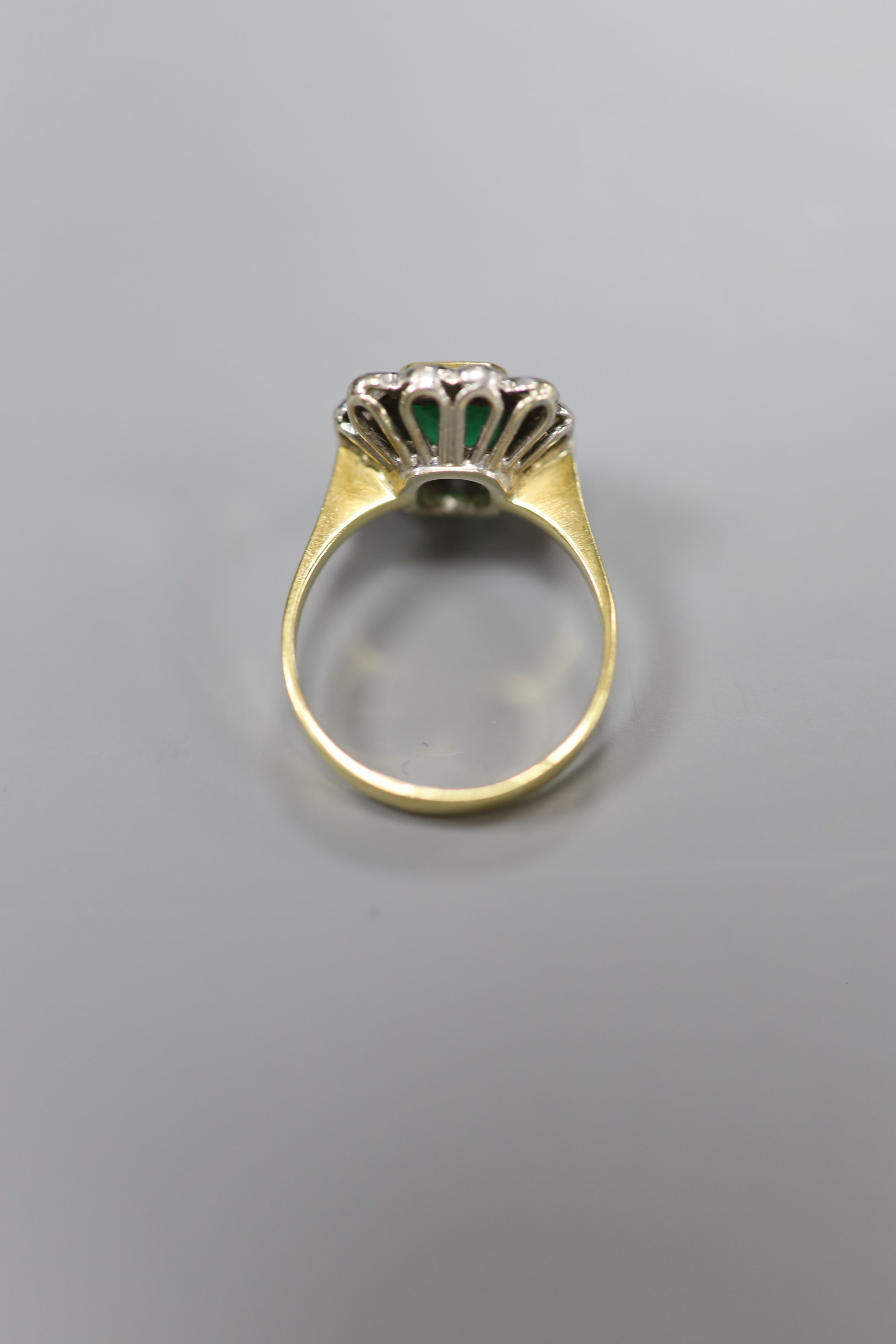 An emerald and diamond cluster ring, white and yellow metal setting (tests as 18ct), size Q, gross 6g.